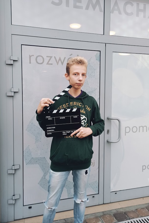 Chłopiec stoi, w ręce trzyma klaps filmowy