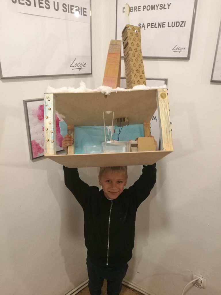 Chłopiec trzyma w górze model swojego miasta z drewna, kartonu i plastiku
