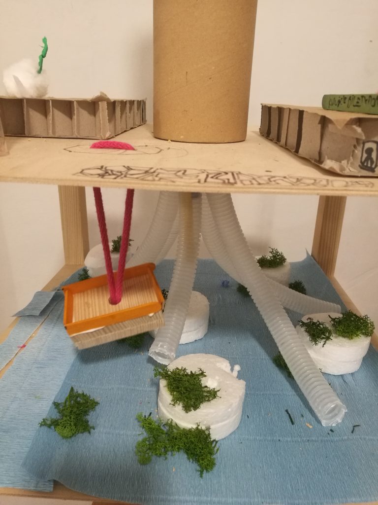 fragment modelu miasta, na nim papierowa tuba, rurki z plastiku, domki z kartonu