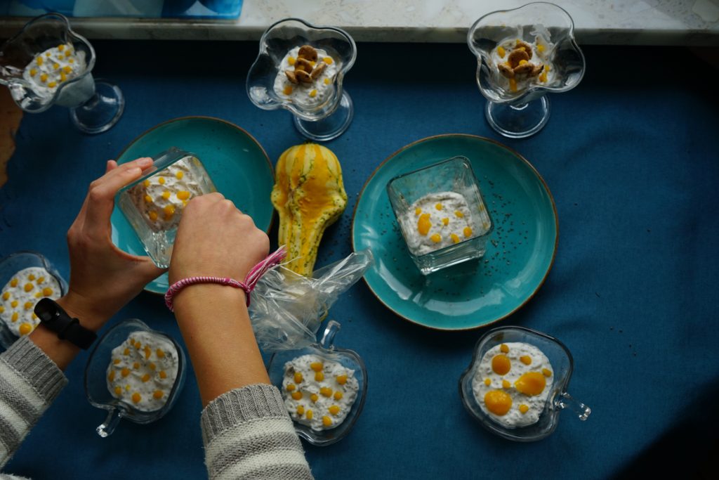 Mleczno-kokosowy deser w szklanych naczyniach, z zatopionymi nasionami chia, dwa talerze z deserami