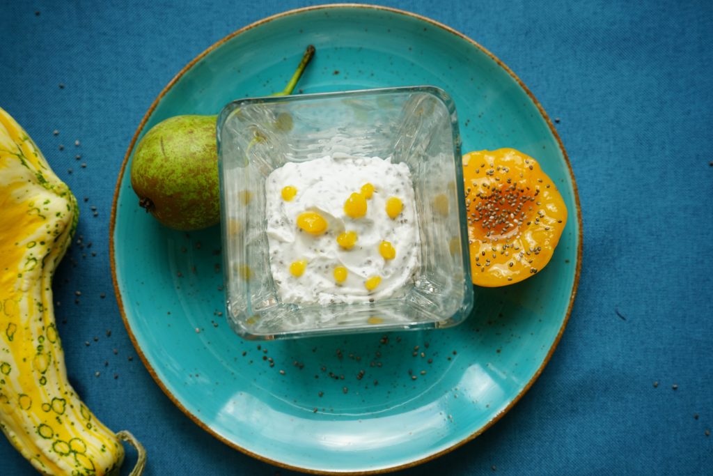 Mleczno-kokosowy deser z zatopionymi nasionami chia, deser podany w szklanym pucharku, na talerzu, obok deseru owoce