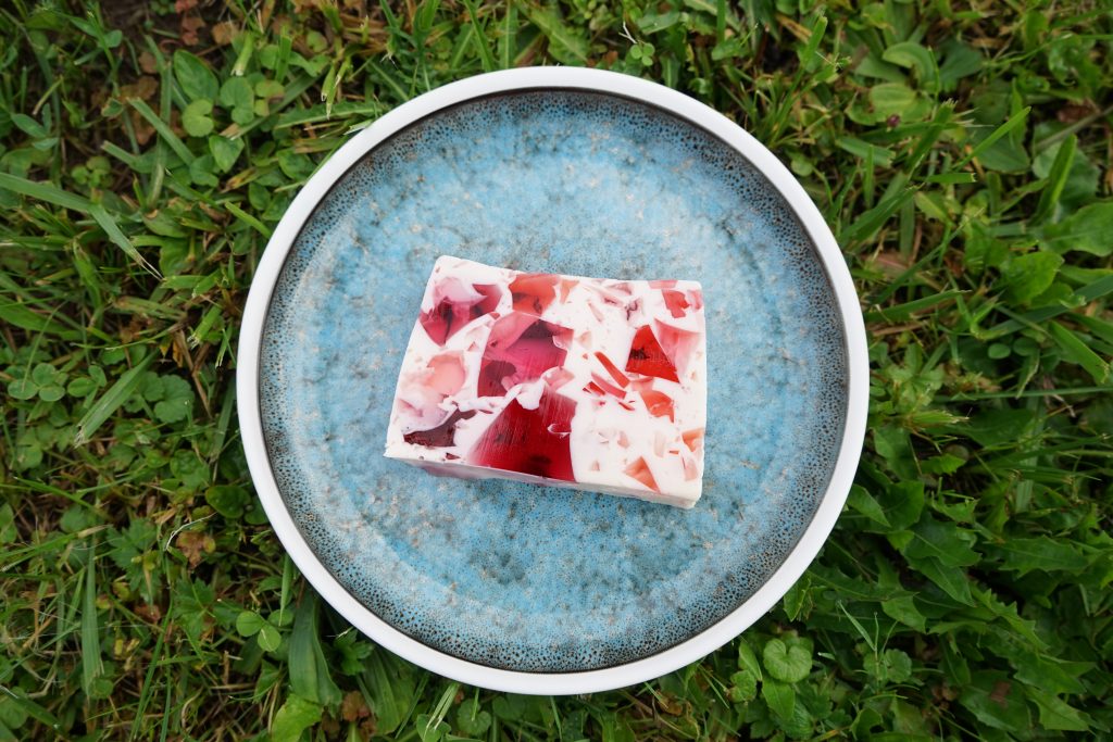 Talerz na trawie, na talerzu deser z białej masy jogurtowej z kawalkami kolorowych glaretek